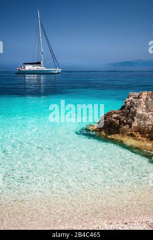 Bella la calma blu azzurro laguna con catamarano a vela yacht barca ad ancoraggio. Bianco puro e sulla spiaggia di ciottoli con rocce in mare. Foto Stock