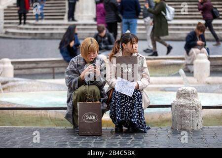 Roma, Italia - 04 Marzo 2020: Turisti cinesi in un momento di pausa dopo lo shopping in Piazza di Spagna, seduti ai margini del fienile della Barcaccia Foto Stock