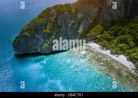 Veduta aerea della spiaggia tropicale con le barche di banca sull'isola di Entalula. Le montagne rocciose di roccia calcarea carsica circondano la baia blu con una splendida barriera corallina. Foto Stock