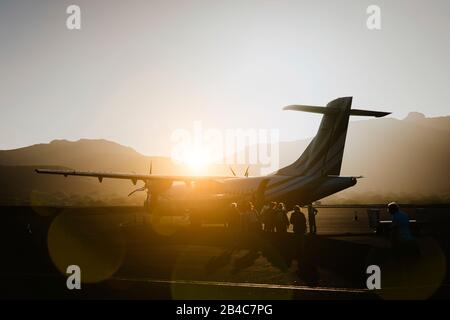 Passeggeri a bordo di un aereo con elica in polverosa mattinata. Catena montuosa che circonda la pista sull'aeroporto Sao Vicente Capo Verde. Foto Stock