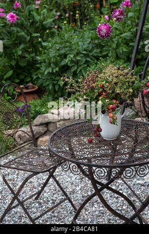 Autunno ancora vita con un bouquet di piante, bacche e piccole mele in una brocca bianca rustica, disposti su un tavolo vintage in un grazioso giardino di campagna Foto Stock