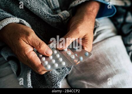 primo piano di mani di uomo anziano che prende o sceglie un cuscino per curare la sua febbre e per essere sano e non malato - pensionato e pensionato da solo a casa - farmacia di solito vita per anziani Foto Stock