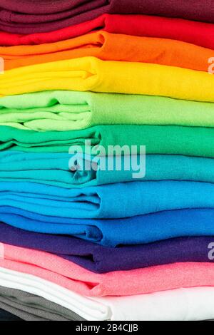 primo piano di molte nuove magliette in cotone in tessuto fresco in colori arcobaleno colorati. Pile di varie camicie colorate di sfondo Foto Stock