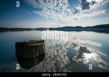 Deadwood sulla riva di un lago con riflessione di belle nuvole nella retroilluminazione Foto Stock