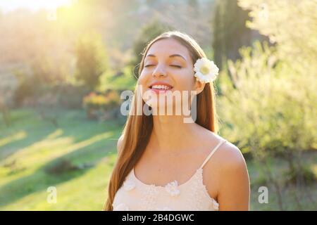 Bella ragazza con occhi chiusi e fiori sull'orecchio sorridente godendo di respirare aria fresca all'aperto