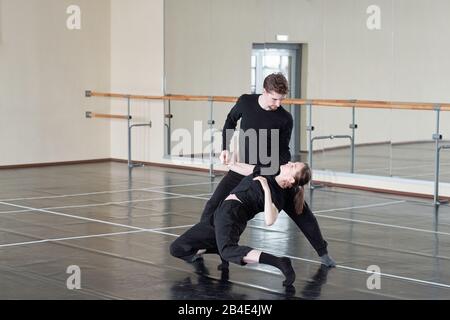 Giovane coppia in pantaloni neri e t-shirt allenare uno di esercizio di danza durante la lezione in grande studio moderno di danza Foto Stock