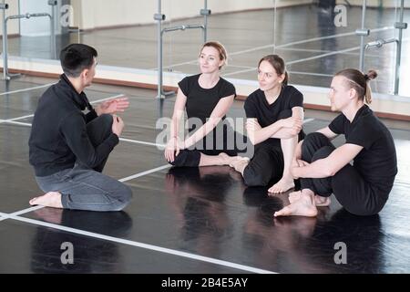 Tre giovani studenti di corso di danza che guardano il loro groupmate durante la discussione di esercizi di base a pausa dopo la formazione Foto Stock