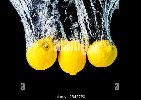 I limoni si tuffano in acqua e affondano su sfondo nero. Foto Stock