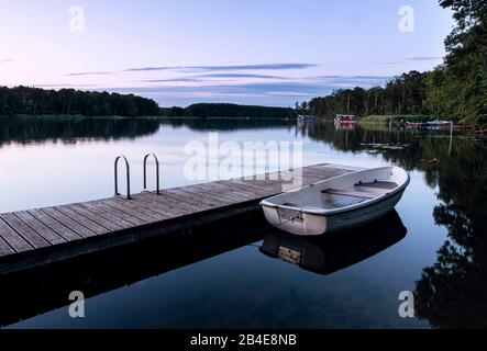 Tranquilla estate sera umore su un lago tedesco orientale. Houseboats sono sulla riva. In primo piano un molo con barca a remi Foto Stock