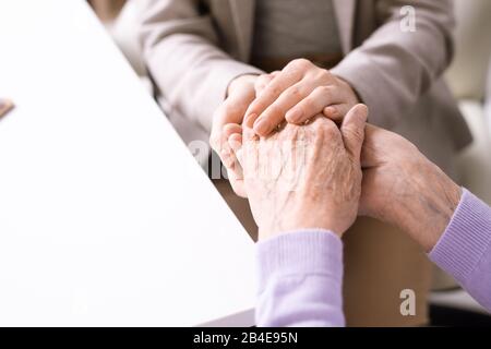 Mani di giovane donna che tiene quelle di una femmina anziana in pensione mentre sostiene e confortano sua madre o nonna Foto Stock