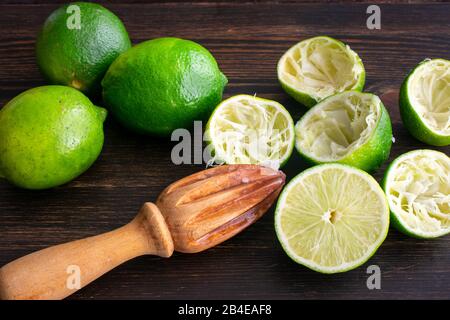 Lime juged su un tagliere di legno: Metà di lime e un alesatore di agrumi su un fondo di legno scuro Foto Stock