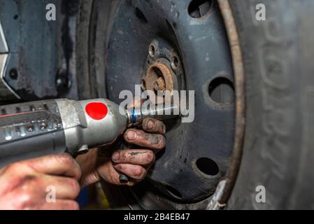 Il meccanico della vettura imbullone il volante della vettura in acciaio con una chiave pneumatica in un'officina, mani maschio visibili. Foto Stock