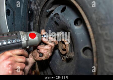 Il meccanico della vettura imbullone il volante della vettura in acciaio con una chiave pneumatica in un'officina, mani maschio visibili. Foto Stock