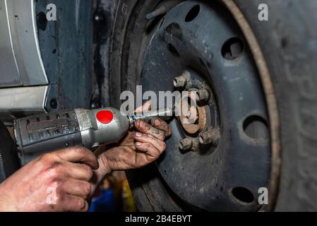 Il meccanico della vettura imbullone il volante della vettura in acciaio con una chiave pneumatica in un'officina, mani maschio visibili. Foto Stock