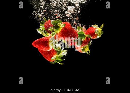 Le fragole di cadere in acqua causando bolle tutto intorno. Cibo sano concetto Foto Stock