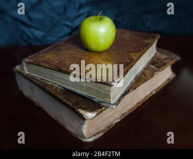 Una mela verde sopra libri antichi. Foto Stock