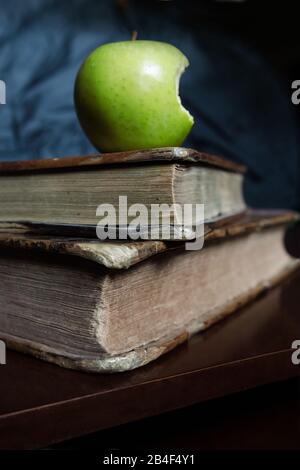 Una mela verde morso sopra libri antichi. Foto Stock