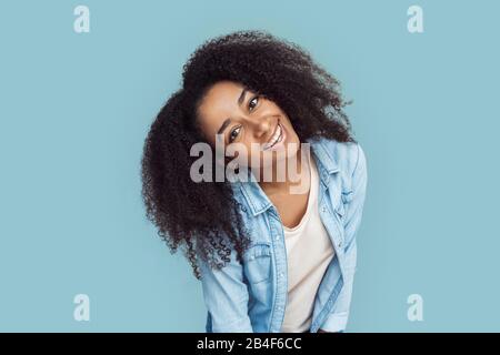 Giovane ragazza africana in piedi isolato su sfondo grigio appoggiandosi in avanti per la telecamera sorridente giocoso primo piano Foto Stock