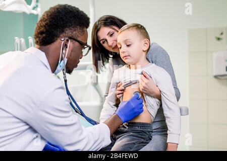 Ragazzino con madre che visita il medico afroamericano dei bambini con stetoscopio in ospedale. Foto Stock