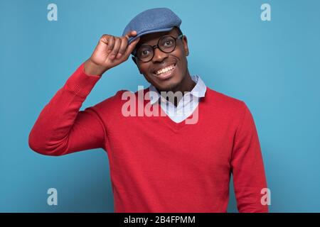 Bell'uomo nero afroamericano in maglione rosso, cappello blu, occhiali sorridenti guardando la macchina fotografica fiducioso. Emozione umana facciale positiva. Foto Stock