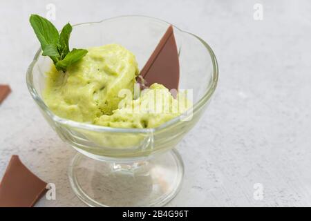 Immagine ravvicinata di un sano gelato avocado in una ciotola di vetro su fondo neutro di cemento Foto Stock