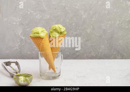 Coni di cialda con gelato facile e sano avocado su sfondo neutro in cemento, spazio di copia Foto Stock
