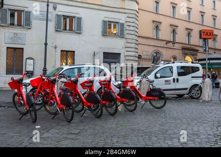 Una fila di biciclette elettriche Uber Jump fiancheggiata da taxi in attesa di passeggeri in una piazza di Roma Foto Stock
