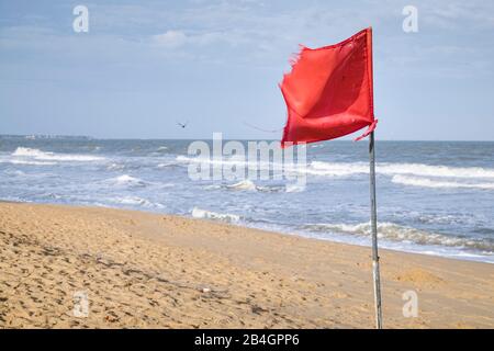 una bandiera rossa sulla spiaggia soffia nel vento Foto Stock