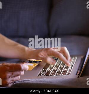 L'uomo ha le mani che tengono la carta di credito, pagano in linea e che immette il codice di sicurezza, usando il computer portatile e sdraiato sul divano di notte, fuoco morbido, spazio di copia Foto Stock