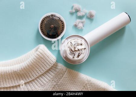 Distaccante per pelucchi/pelucchi da un pullover bianco in acrilico o lana. Dispositivo elettrico dopo la pulizia e raccolta lanugine/lanugine su sfondo azzurro. Vista dall'alto Foto Stock