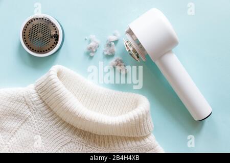 Pilling/Rimozione di pelucchi da un pullover bianco in acrilico o lana. Dispositivo elettrico dopo la pulizia e raccolta lanugine/lanugine su sfondo azzurro. Top vie Foto Stock