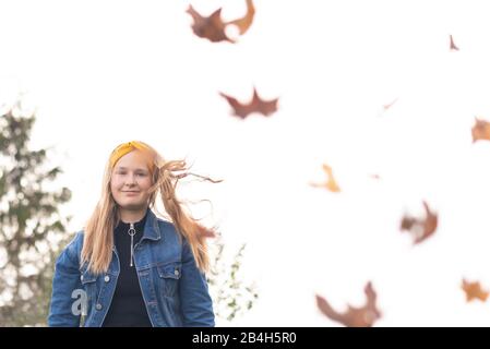 Una ragazza di dodici anni con una fascia gialla è felice circa l'autunno, foglie colorate volare attraverso l'aria Foto Stock