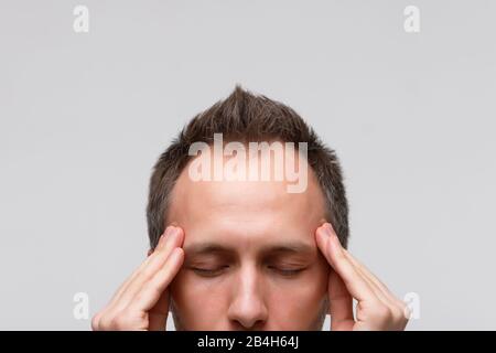 Mal di testa, concetto di tensione nervosa. Primo piano ritratto dell'uomo cerca di concentrarsi, raccogliere con pensieri, meditare e massaggiare i suoi templi, chiuso Foto Stock