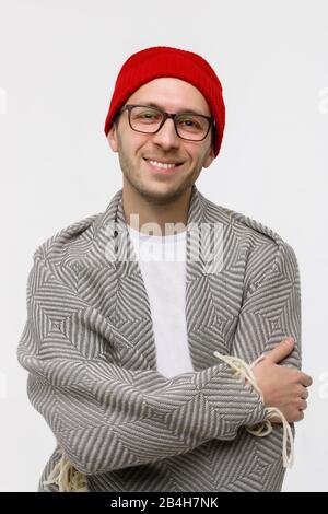 Studio ritratto di allegro ragazzo elegante hippster con setole chiare sul viso sorridente alla fotocamera, indossando occhiali, berretto rosso e avvolto in plaid, un Foto Stock
