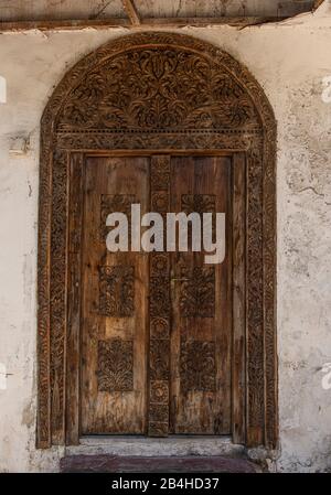 Destinazione Tanzania, Isola di Zanzibar: Impressioni da Stone Town, il più antico distretto di Zanzibar, la capitale dello stato tanzaniano di Zanzibar. Porta in legno con arco rotondo. Foto Stock