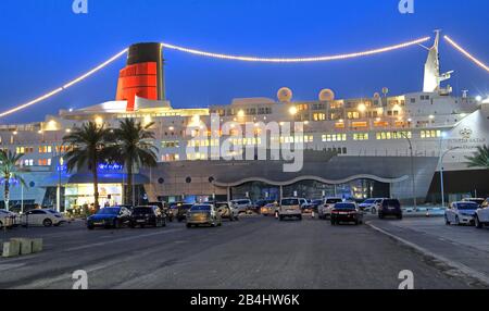 Hotel illuminato e nave museo Regina Elisabetta 2 (QE2) al molo al tramonto, Dubai, Golfo Persico, Emirati Arabi Uniti Foto Stock