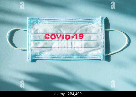 Covid-19 - Il Romanzo di Wuhan Coronavirus polmonite ottiene il nome ufficiale DA CHI: COVID-19. Medicazione monouso sul viso. Contesto sanitario. Maschera facciale monouso per uso medico blu con stampa covid-19 Foto Stock