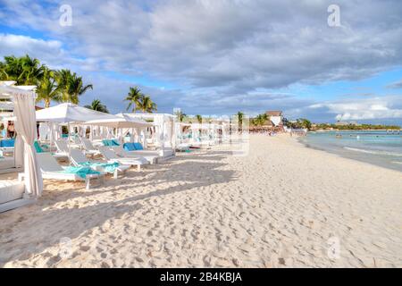 File di letti e sedie su una spiaggia tropicale soleggiata e sabbiosa sulla costa caraibica di Cancun, Messico. Concetto di vacanza estiva o vacanza invernale divertimento. Foto Stock