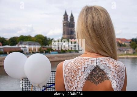 Junge Frau, biondo Haare, schaut bei einem Diner en Blanc auf den Dom a Magdeburg, trägt auf dem Rücken ein Tattoo. Foto Stock