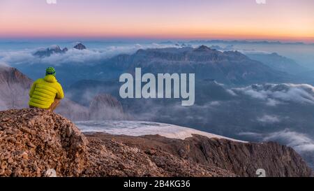 L'alpinista ammira il paesaggio montano all'alba da uno sperone roccioso vicino a Punta Penia, Marmolada, Belluno e Trento, Dolomiti, Italia Foto Stock