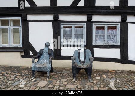 Germania, Bassa Sassonia, Harz, Goslar, casa a graticcio con due sedili in legno che simboleggiano una donna e un uomo. Foto Stock