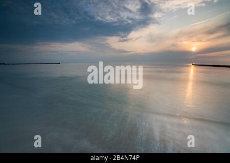 Der Strand an der Ostsee mit Spiegelung der schönen Wolken und Buhnen, die in den das Meer führen im Abendlicht Foto Stock