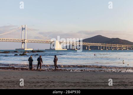 Busan, Corea del Sud - 16 marzo 2018: Gli uomini sono sulla spiaggia con Gwangandaegyo o Diamond Bridge sullo sfondo Foto Stock