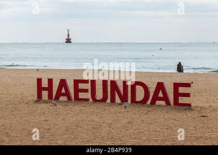 Busan, Corea del Sud - 17 marzo 2018: Haeundae Beach red name text montato sulla costa sabbiosa, gente comune cammina sulla costa sabbiosa Foto Stock