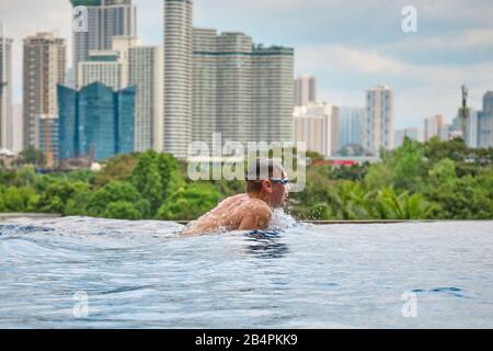 Un uomo nuota una farfalla in una piscina sul tetto di un hotel di lusso. Vista della città di Manila dalla piscina del lussuoso cinque stelle Discovery Primea calda Foto Stock