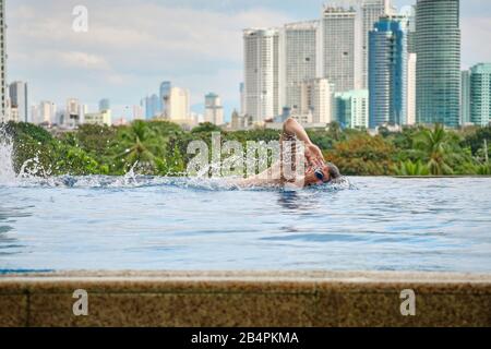 Un uomo nuota una farfalla in una piscina sul tetto di un hotel di lusso. Vista della città di Manila dalla piscina del lussuoso cinque stelle Discovery Primea calda Foto Stock