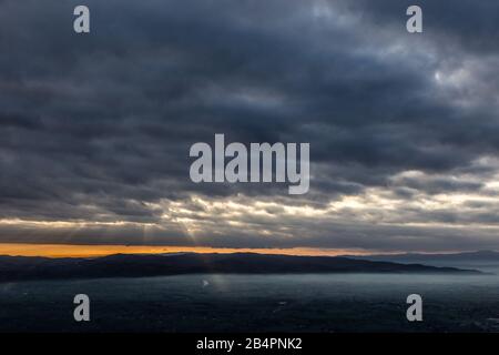 Raggi di sole che scende da alcune nuvole sopra una valle piena di nebbia, illuminando una parte di esso Foto Stock