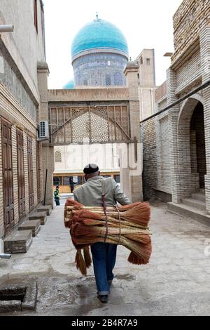 Uomo che porta pile di scopa in vendita sulla strada laterale nel centro storico di Bukhara, Uzbekistan Foto Stock