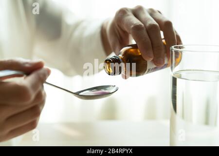 La donna versa manualmente le medicine o tosse sciroppo da bottiglia a cucchiaio. Il concetto di assistenza sanitaria Foto Stock