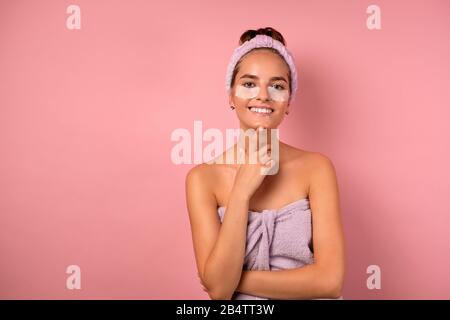 Una ragazza con un bendaggio sulla sua testa e cerotti sotto i suoi occhi si leva in piedi su uno sfondo rosa, propping il suo mento con il dito Foto Stock